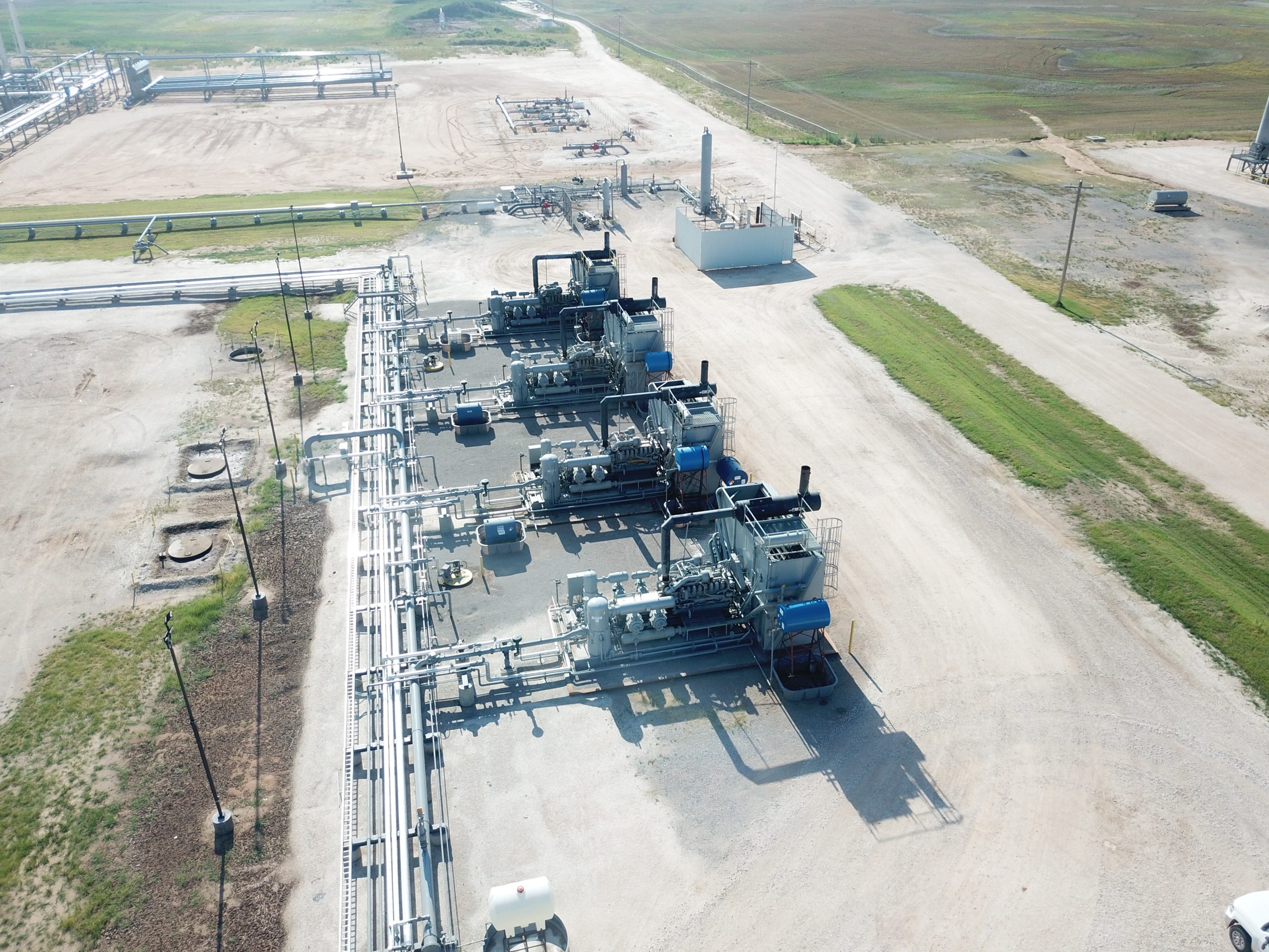 Aerial view of a natural gas processing plant, showing pipelines, equipment, and surrounding landscape on a clear day.