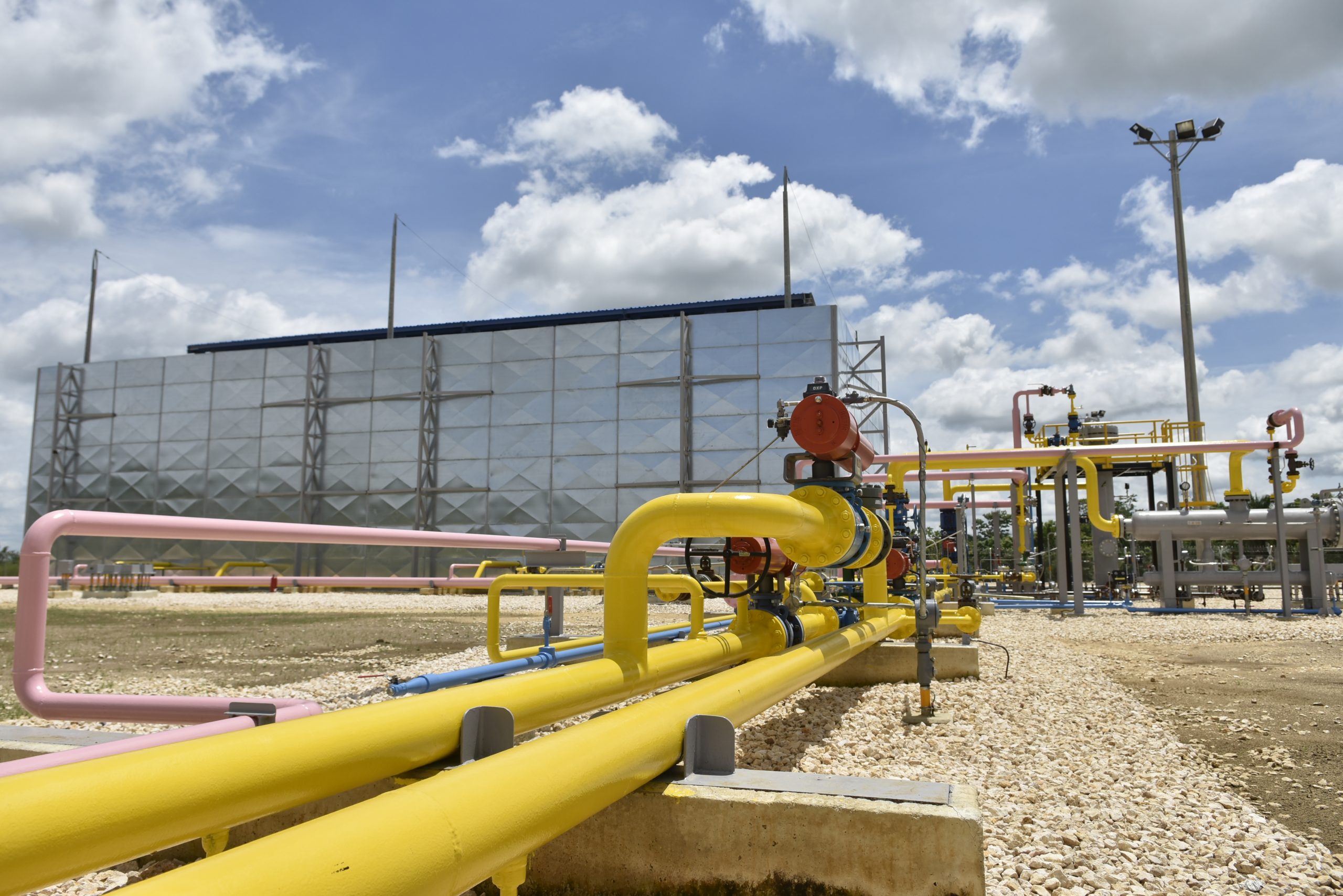 Industrial gas pipeline system with colorful pipes and valves at a natural gas processing plant under a cloudy sky.