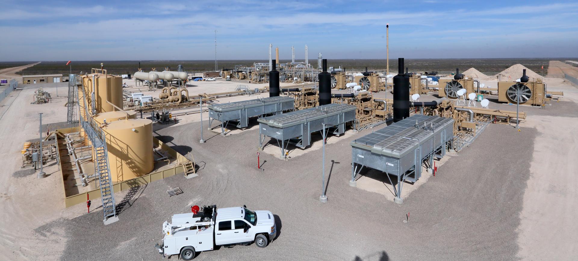 Panoramic view of an industrial gas processing plant with storage tanks, pipelines, and a service truck on a clear day.