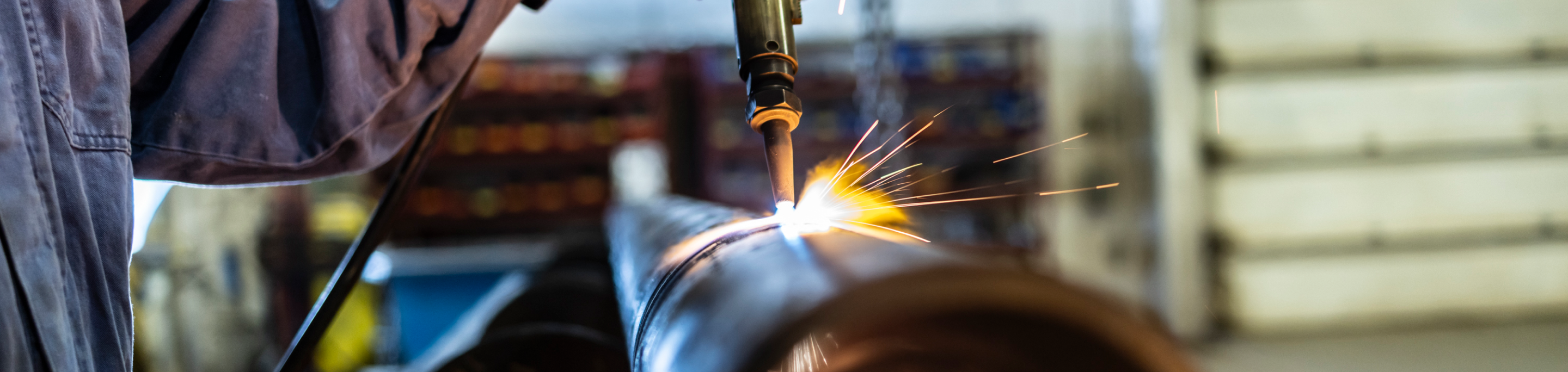 Worker welding metal pipes in an industrial workshop, sparks flying from the welding torch in close-up view.