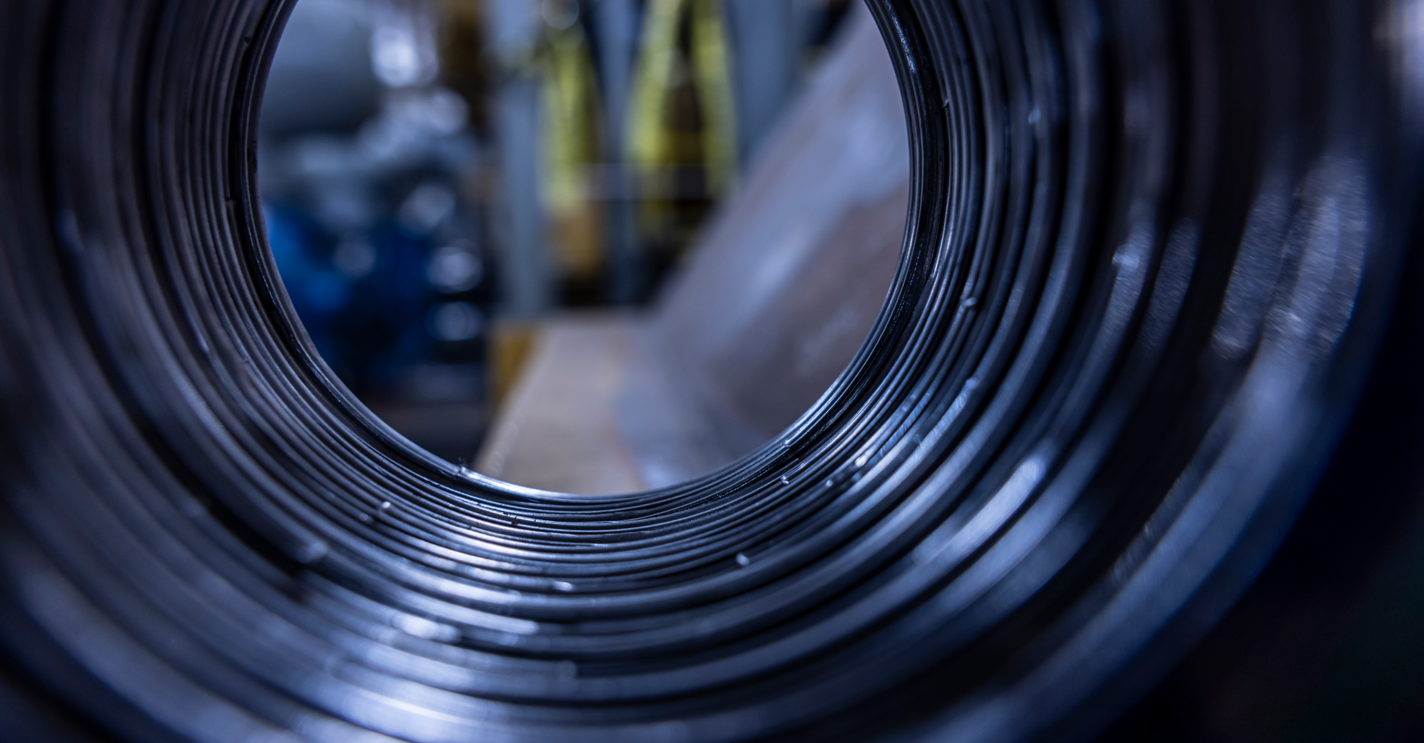 Close-up view inside an industrial metal coil, with blurred factory background, highlighting circular pattern and texture.