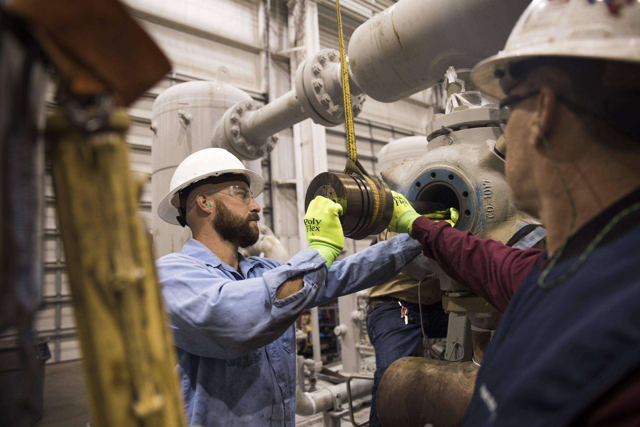 Workers in safety gear maintaining industrial machinery in a factory setting for efficient operations.