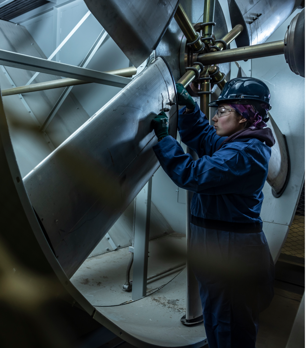 Engineer in safety gear inspecting large industrial fan blades in a factory setting.
