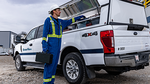 Technician in safety gear accessing equipment from a white Enerflex service truck at an industrial site.